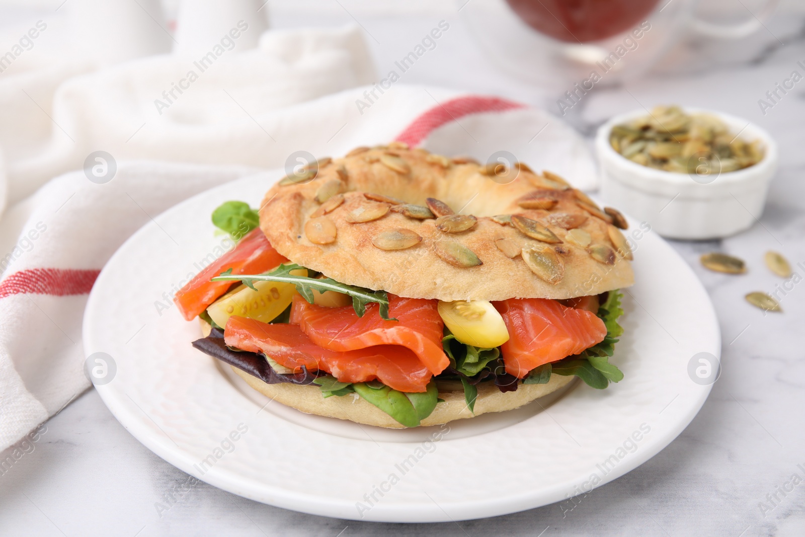 Photo of Tasty bagel with salmon and tomatoes on white marble table, closeup