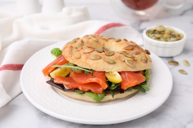 Tasty bagel with salmon and tomatoes on white marble table, closeup