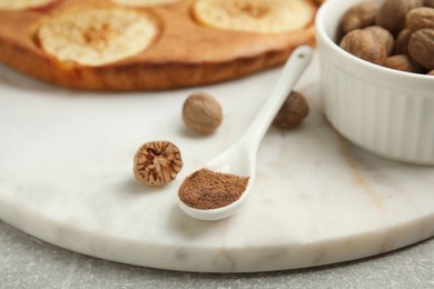 Photo of Nutmeg powder, seeds and tasty pie on light grey table, closeup