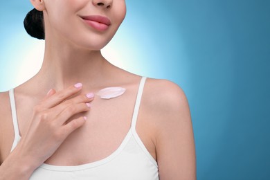 Photo of Woman with smear of body cream on her collarbone against light blue background, closeup. Space for text