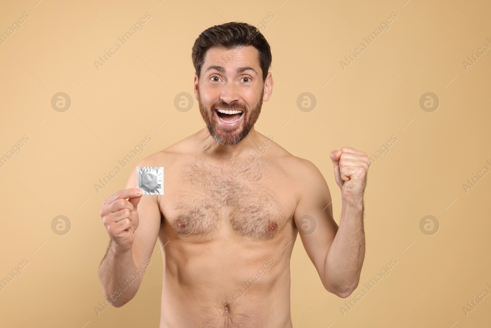 Photo of Emotional naked man holding condom on beige background. Safe sex