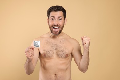Emotional naked man holding condom on beige background. Safe sex