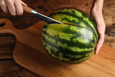 Photo of Woman cutting delicious watermelon at wooden table, closeup