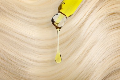 Image of Dripping cosmetic oil from pipette onto blonde hair, closeup