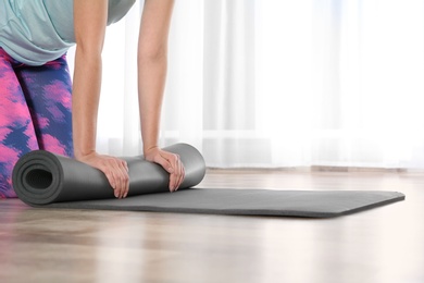 Photo of Woman rolling yoga mat on floor indoors, closeup. Space for text