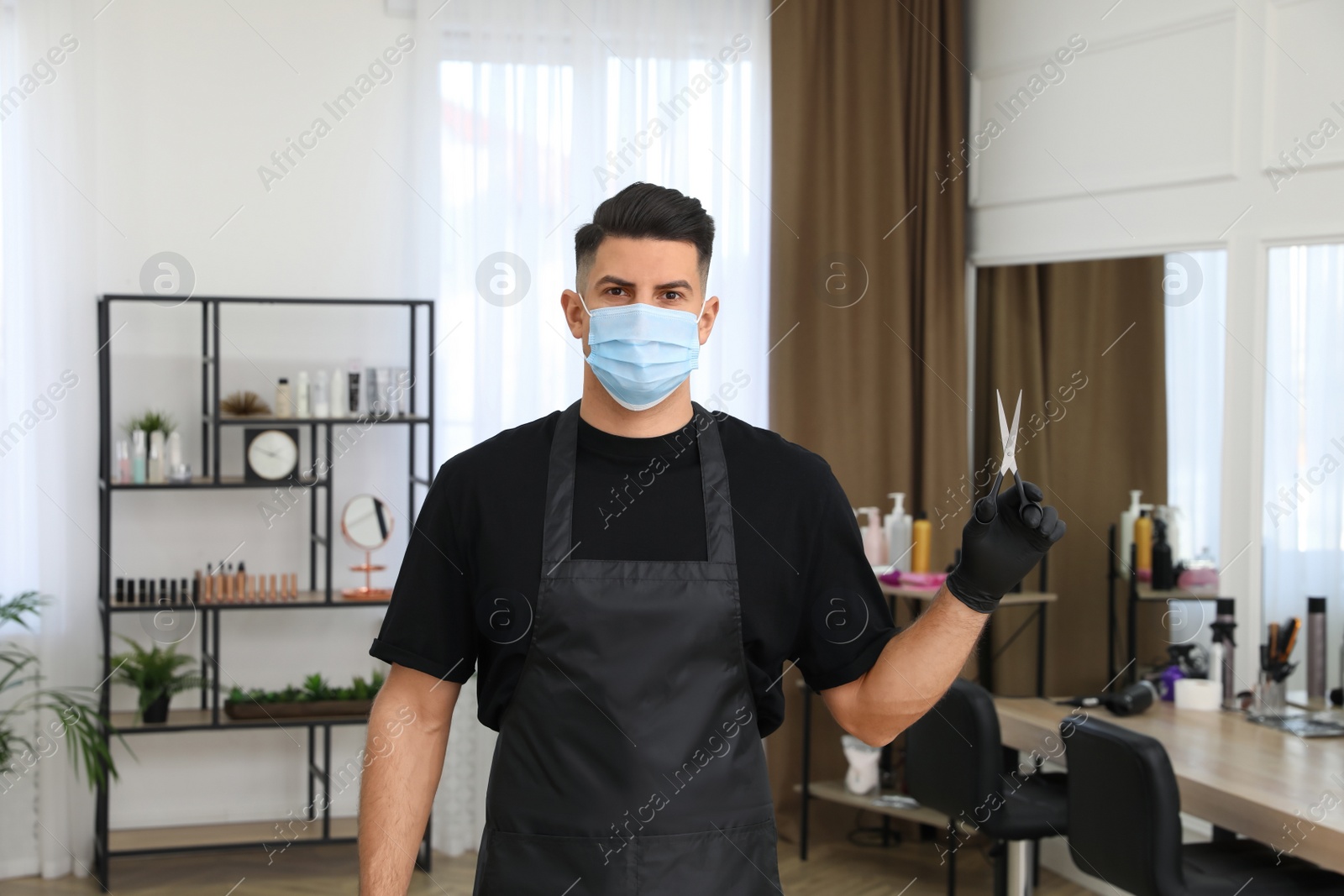Photo of Professional stylist in protective mask holding scissors indoors. Hairdressing services during Coronavirus quarantine
