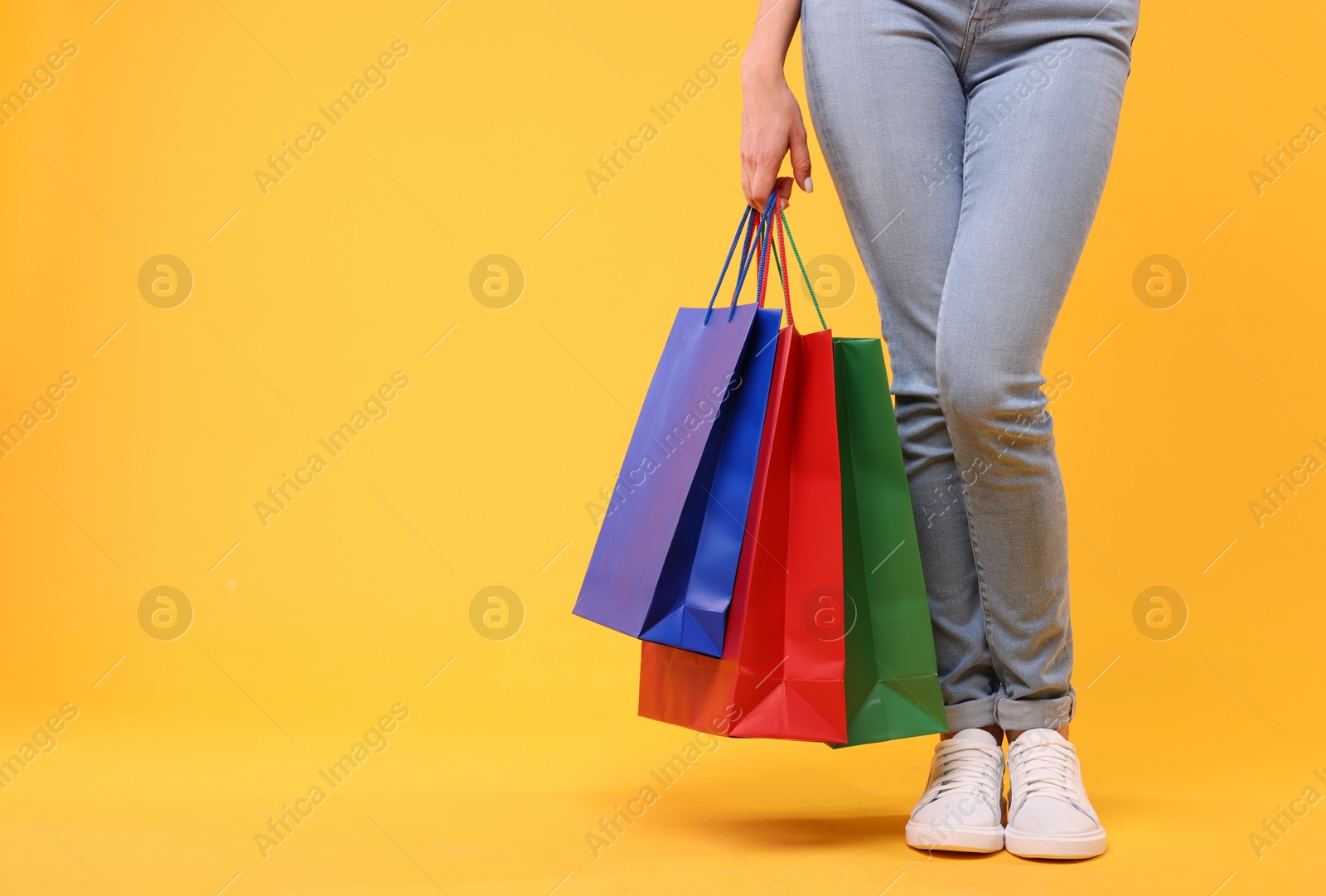 Photo of Woman with shopping bags on yellow background, closeup. Space for text