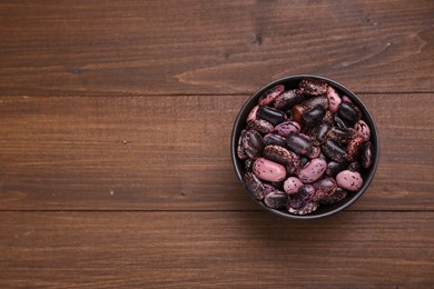 Photo of Bowl with dry kidney beans on wooden table, top view. Space for text