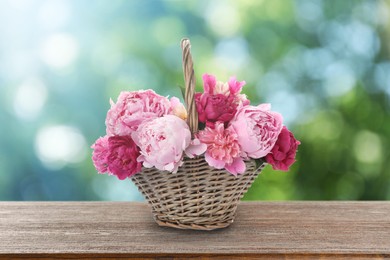 Image of Wicker basket with beautiful pink peonies on wooden table outdoors. Bokeh effect