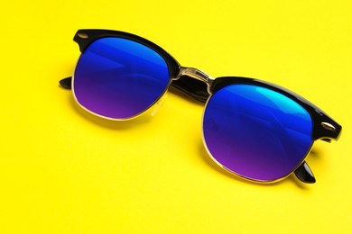 New stylish elegant sunglasses with color lenses on yellow background