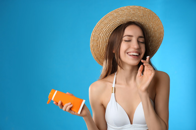 Young woman applying sun protection cream on light blue background