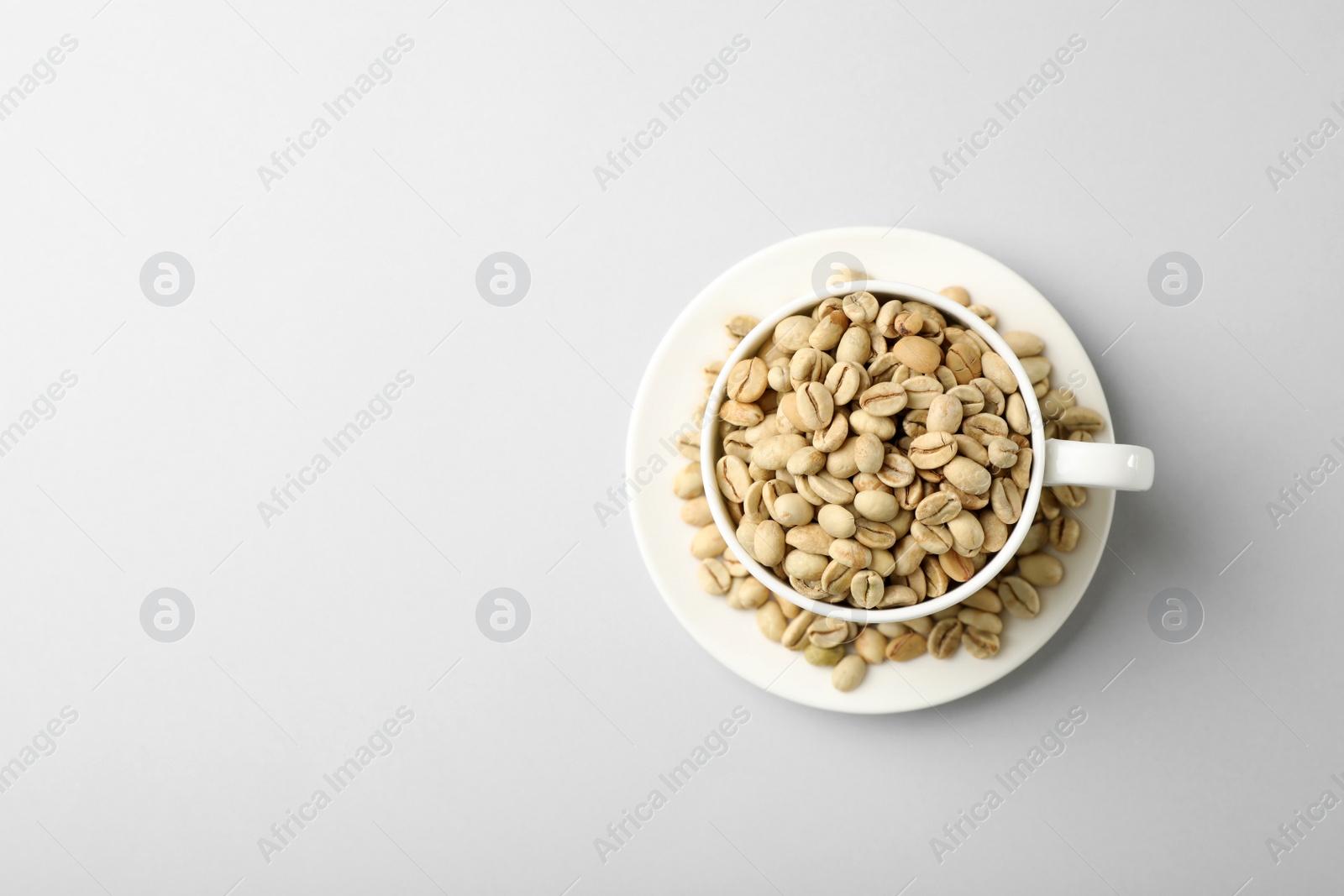 Photo of Cup and saucer with green coffee beans on white background, top view. Space for text