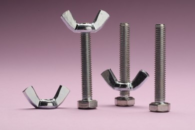 Photo of Three metal screws with wing nuts on purple background