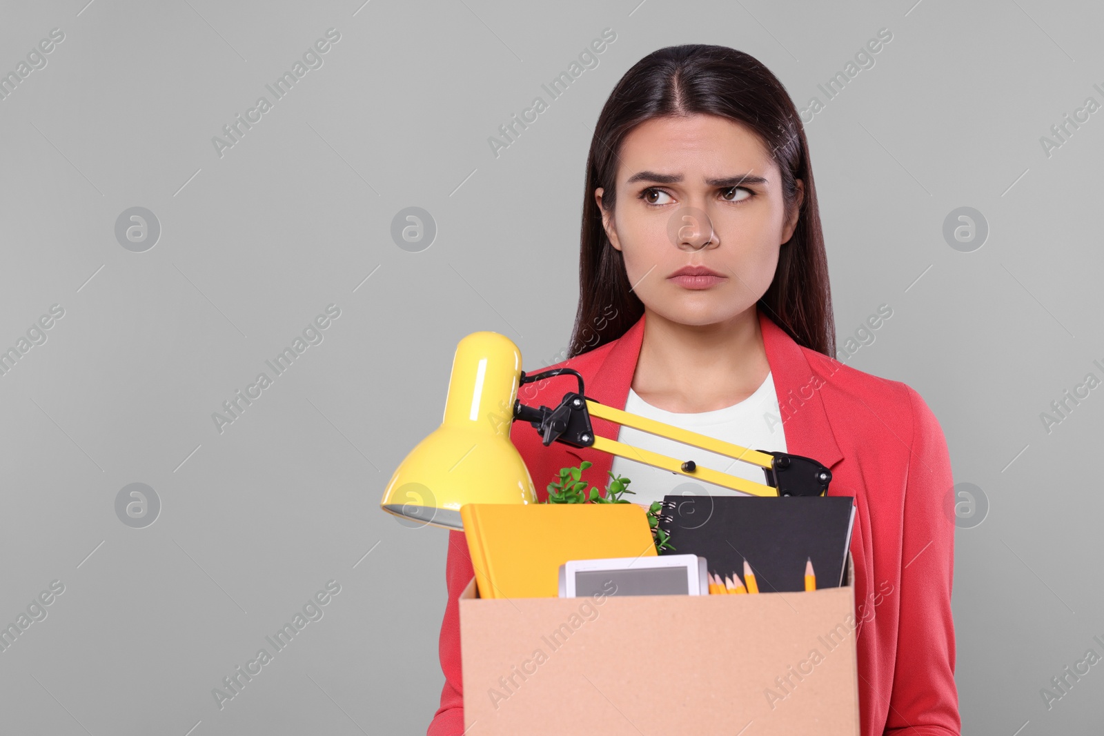 Photo of Unemployed woman with box of personal office belongings on grey background. Space for text