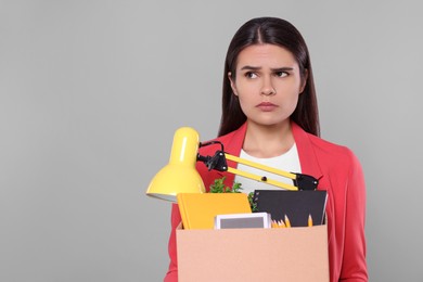 Photo of Unemployed woman with box of personal office belongings on grey background. Space for text