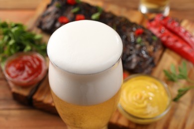 Photo of Glass of beer, tasty grilled ribs and sauces on table, closeup