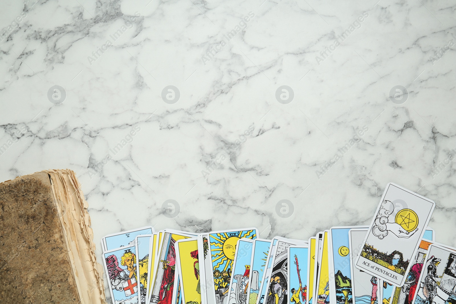 Photo of Tarot cards and old book on white marble table, flat lay. Space for text
