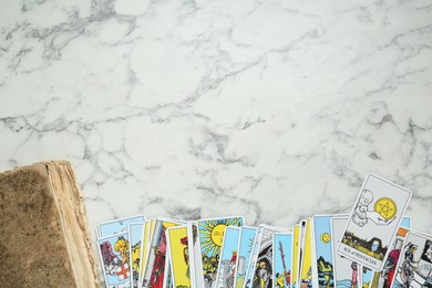 Tarot cards and old book on white marble table, flat lay. Space for text