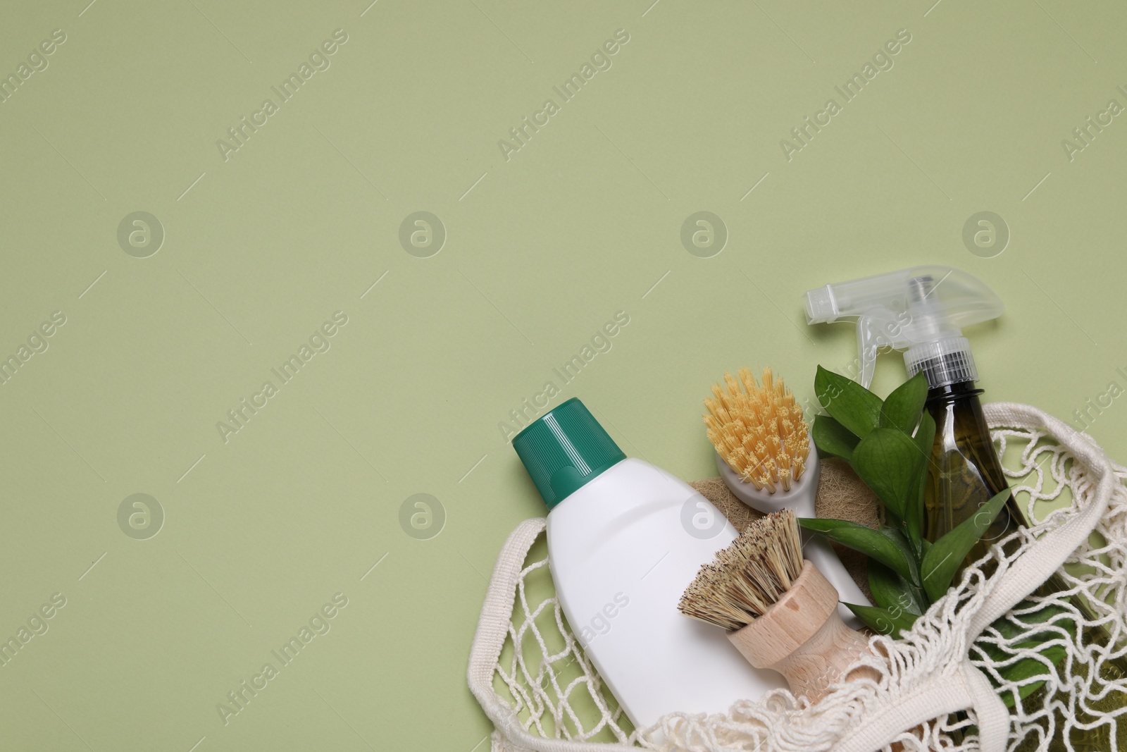 Photo of Different cleaning supplies in string bag on green background, space for text