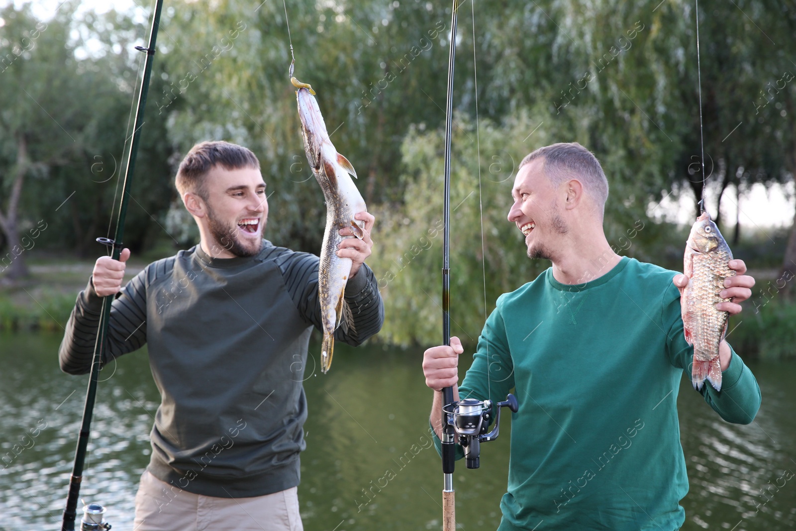 Photo of Friends with fishing rods and catch at riverside. Recreational activity