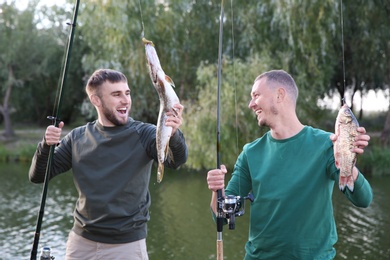 Friends with fishing rods and catch at riverside. Recreational activity