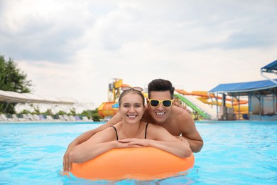 Happy couple with inflatable ring in swimming pool at water park