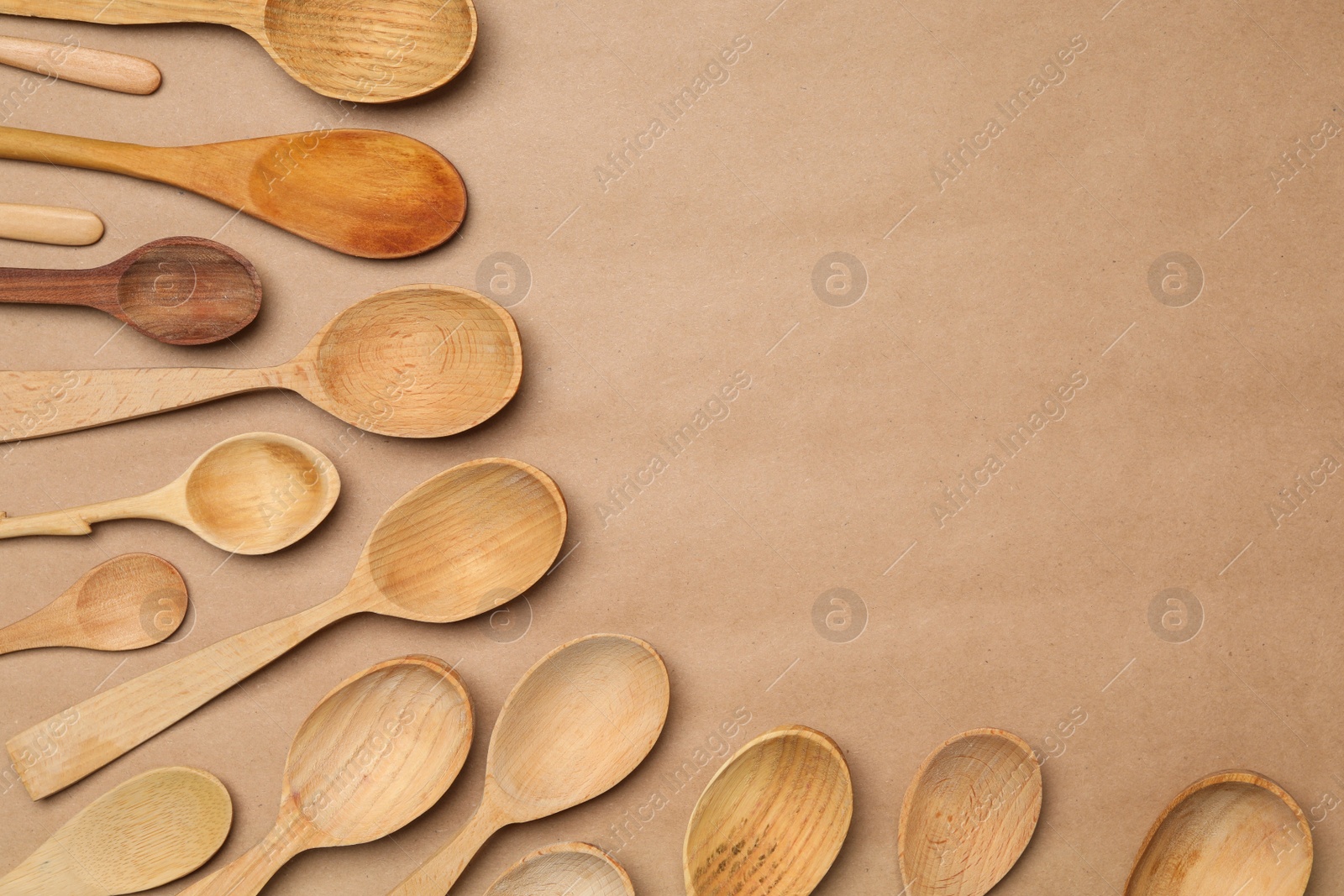 Photo of New wooden spoons on brown background, flat lay with space for text. Cooking utensils