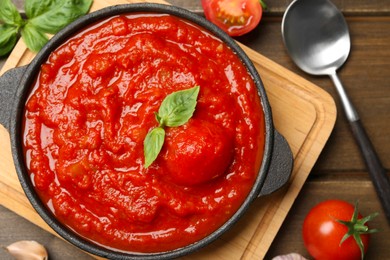 Homemade tomato sauce in bowl, spoon and ingredients on wooden table, flat lay