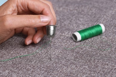 Photo of Woman sewing on grey fabric with thimble and needle, closeup