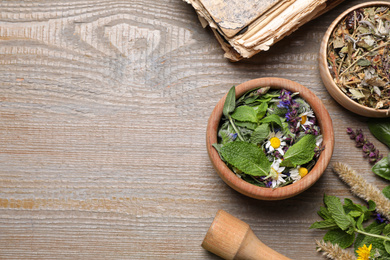 Photo of Flat lay composition with mortar and different healing  herbs on wooden table, space for text