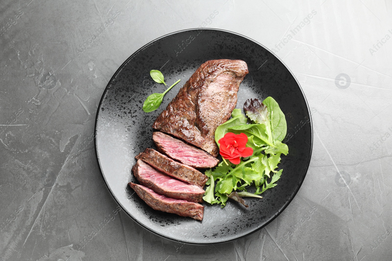 Photo of Pieces of delicious grilled beef meat and greens on grey table, top view