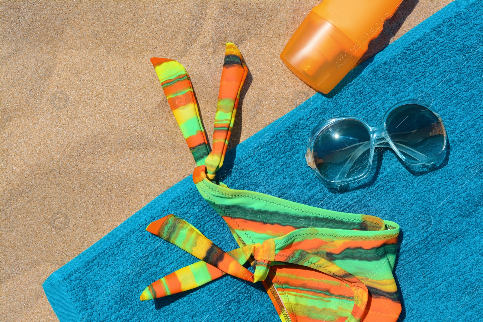 Photo of Soft blue beach towel with bottle of sunscreen, sunglasses and colorful bikini bottom, flat lay