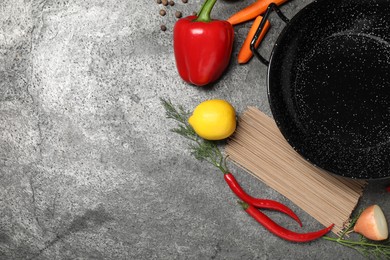 Empty iron wok and raw ingredients on grey table, flat lay. Space for text