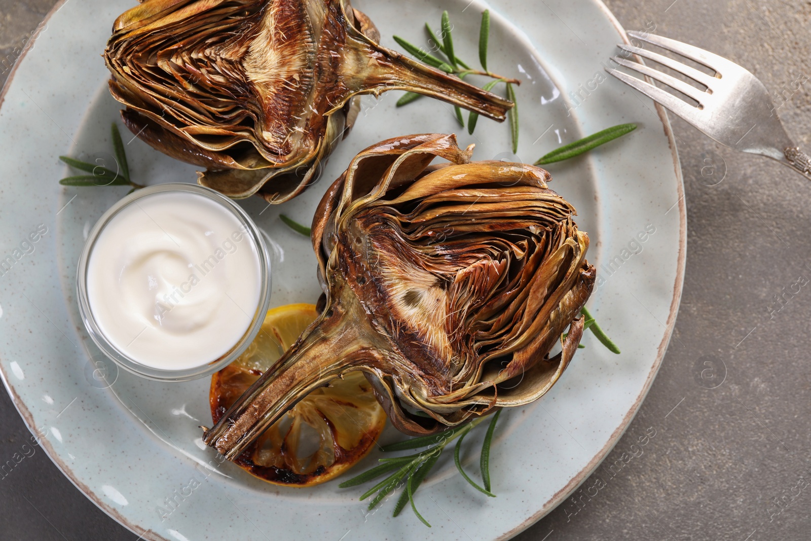 Photo of Plate with tasty grilled artichoke served on grey table, top view