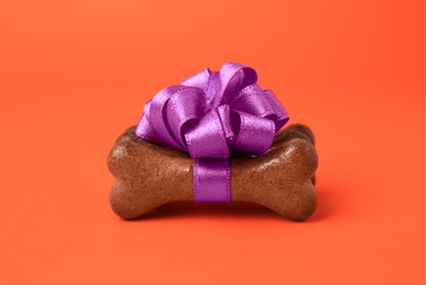 Photo of Bone shaped dog cookies with purple bow on orange background, closeup