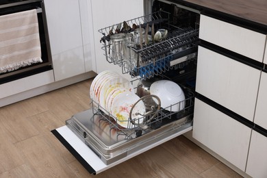 Photo of Open modern dishwasher with dirty tableware in kitchen