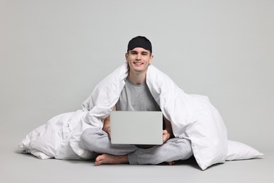Happy man in pyjama wrapped in blanket using laptop on grey background