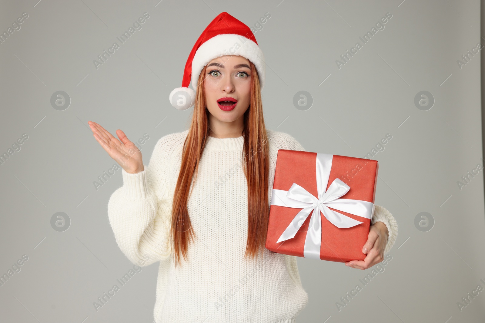 Photo of Emotional young woman in Santa hat with Christmas gift on light grey background