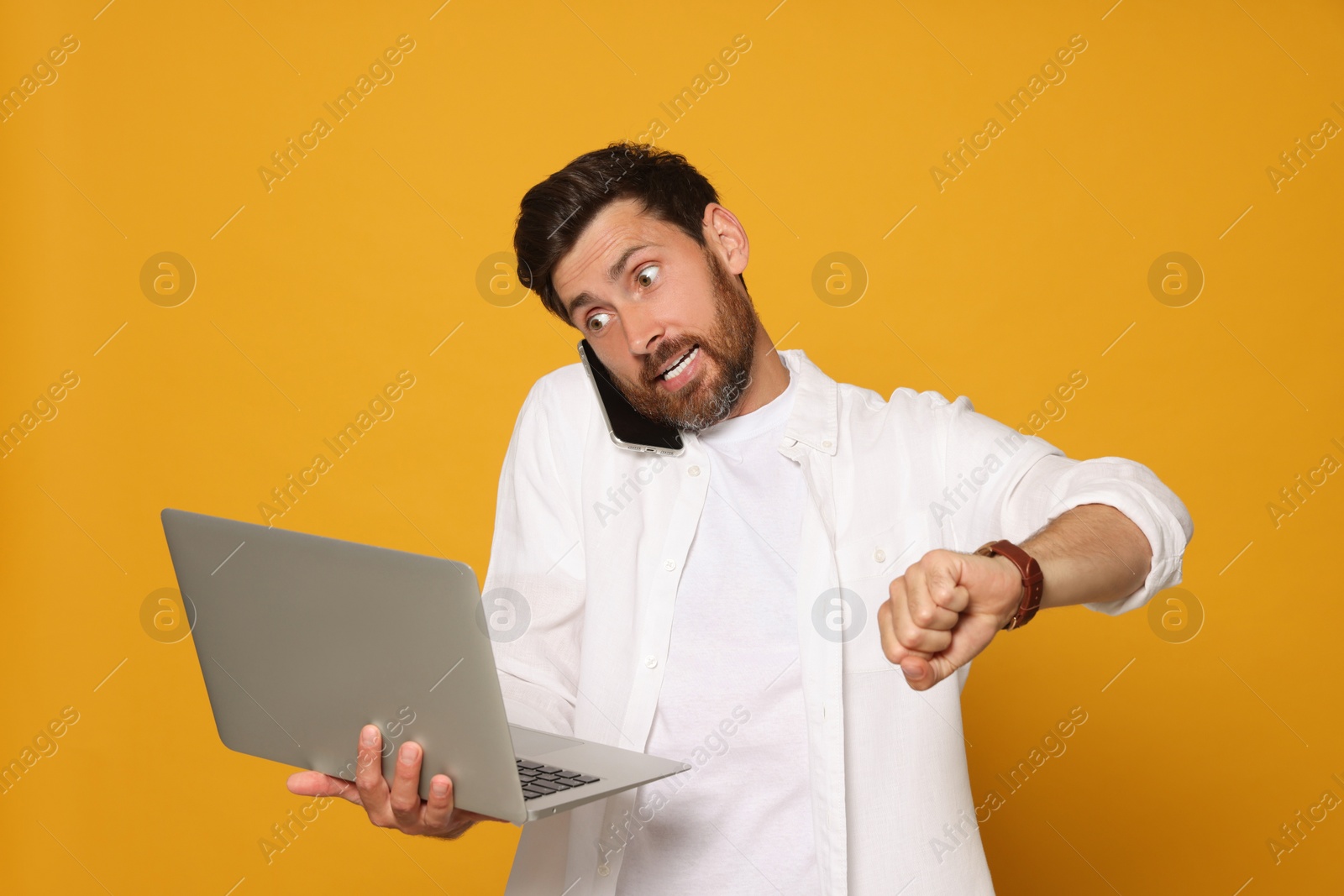 Photo of Emotional man with laptop talking on phone against orange background. Being late concept