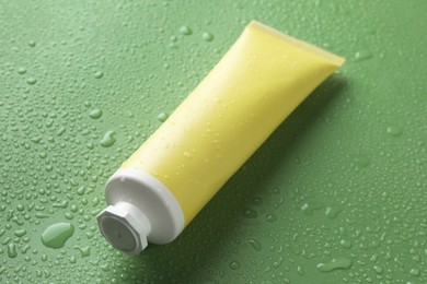 Moisturizing cream in tube on green background with water drops, closeup