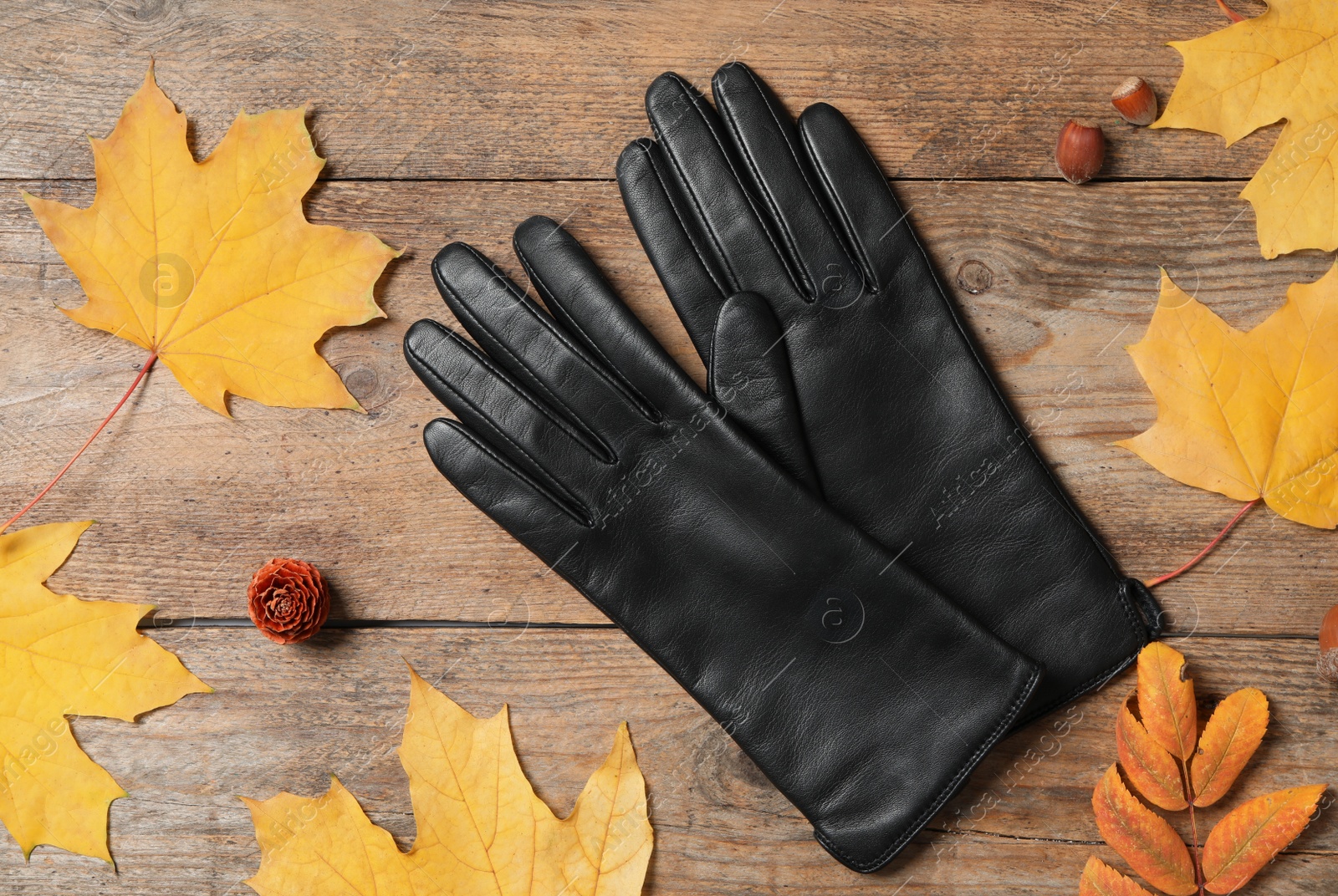 Photo of Stylish black leather gloves and dry leaves on wooden table, flat lay