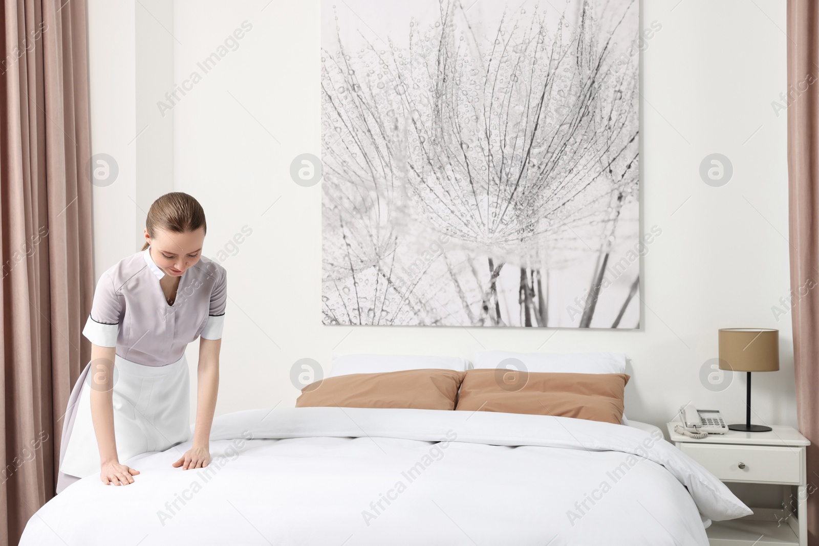 Photo of Young maid making bed in hotel room. Space for text