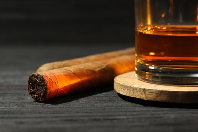 Photo of Glass of whiskey and cigars on black wooden table, closeup