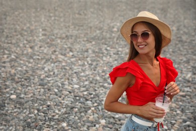 Beautiful young woman with tasty milk shake on beach, space for text