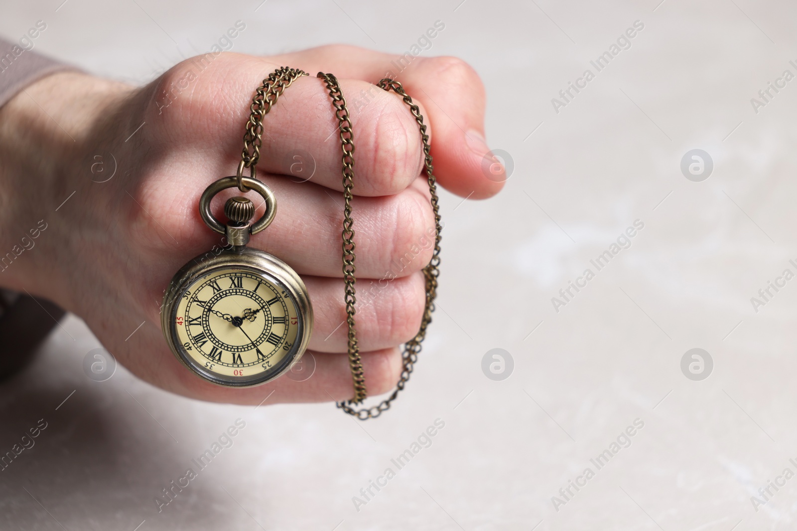 Photo of Man holding chain with elegant pocket watch at light marble table, closeup. Space for text