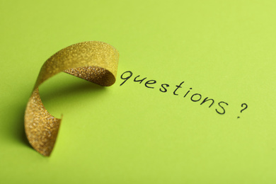 Photo of Word QUESTIONS and shiny ribbon on green background, closeup