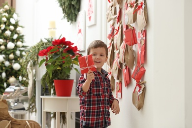 Photo of Cute little boy taking gift from Advent calendar at home. Christmas tradition