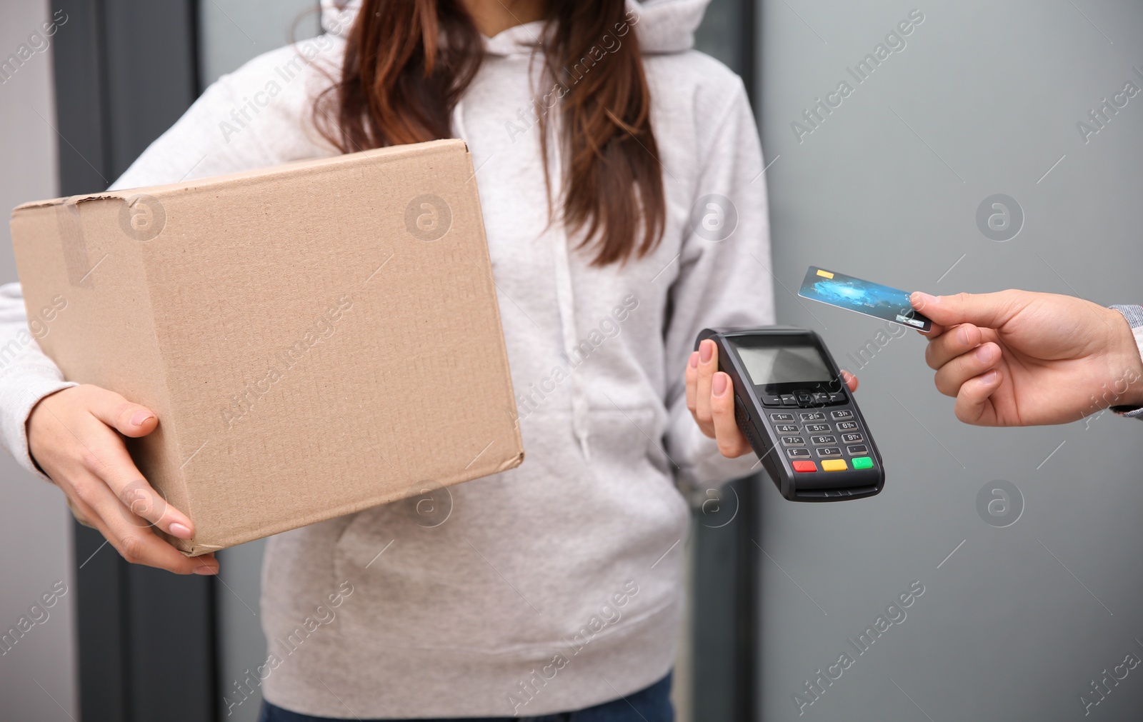 Photo of Young man with credit card using bank terminal for delivery payment at doorway, closeup