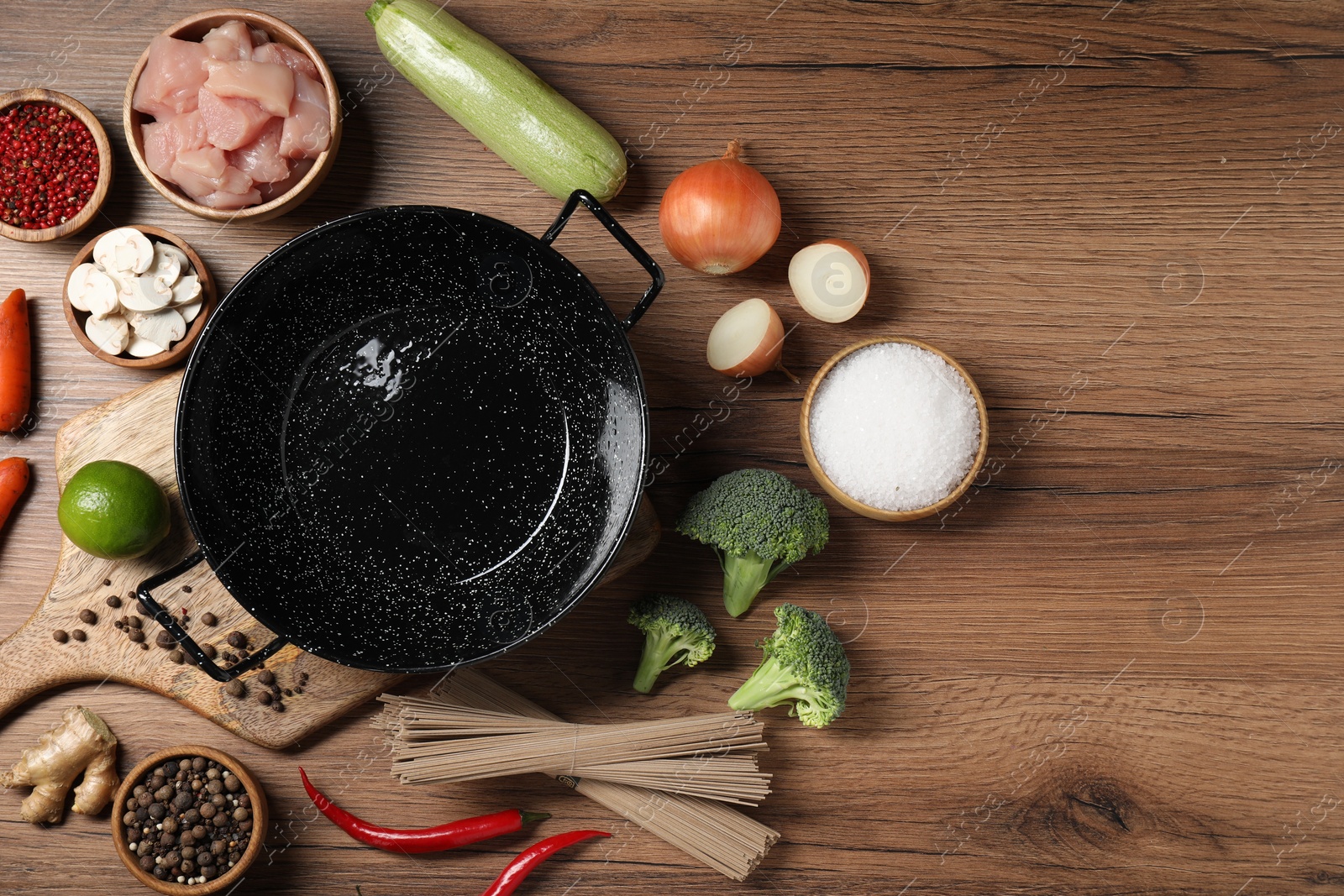 Photo of Empty iron wok surrounded by raw ingredients on wooden table, flat lay. Space for text