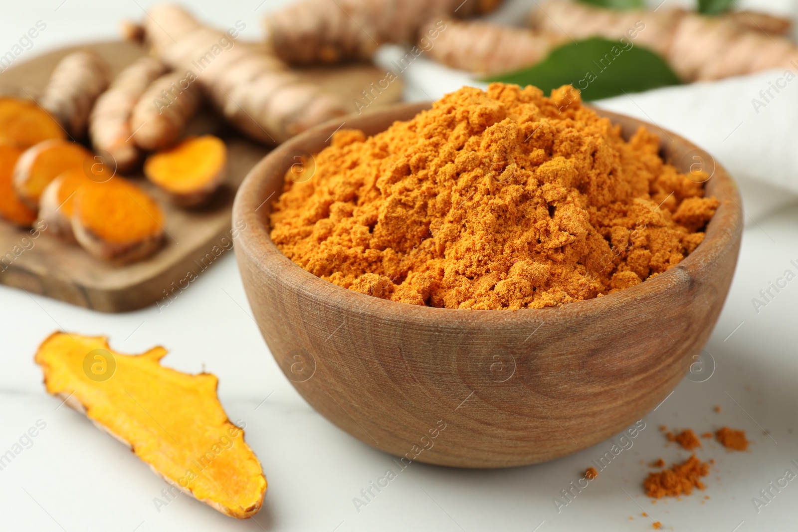 Photo of Aromatic turmeric powder and raw roots on white table, closeup